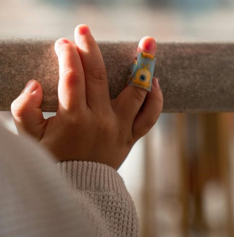 A close-up of a child's hand with a colorful bandage, resting on a poolside ledge.